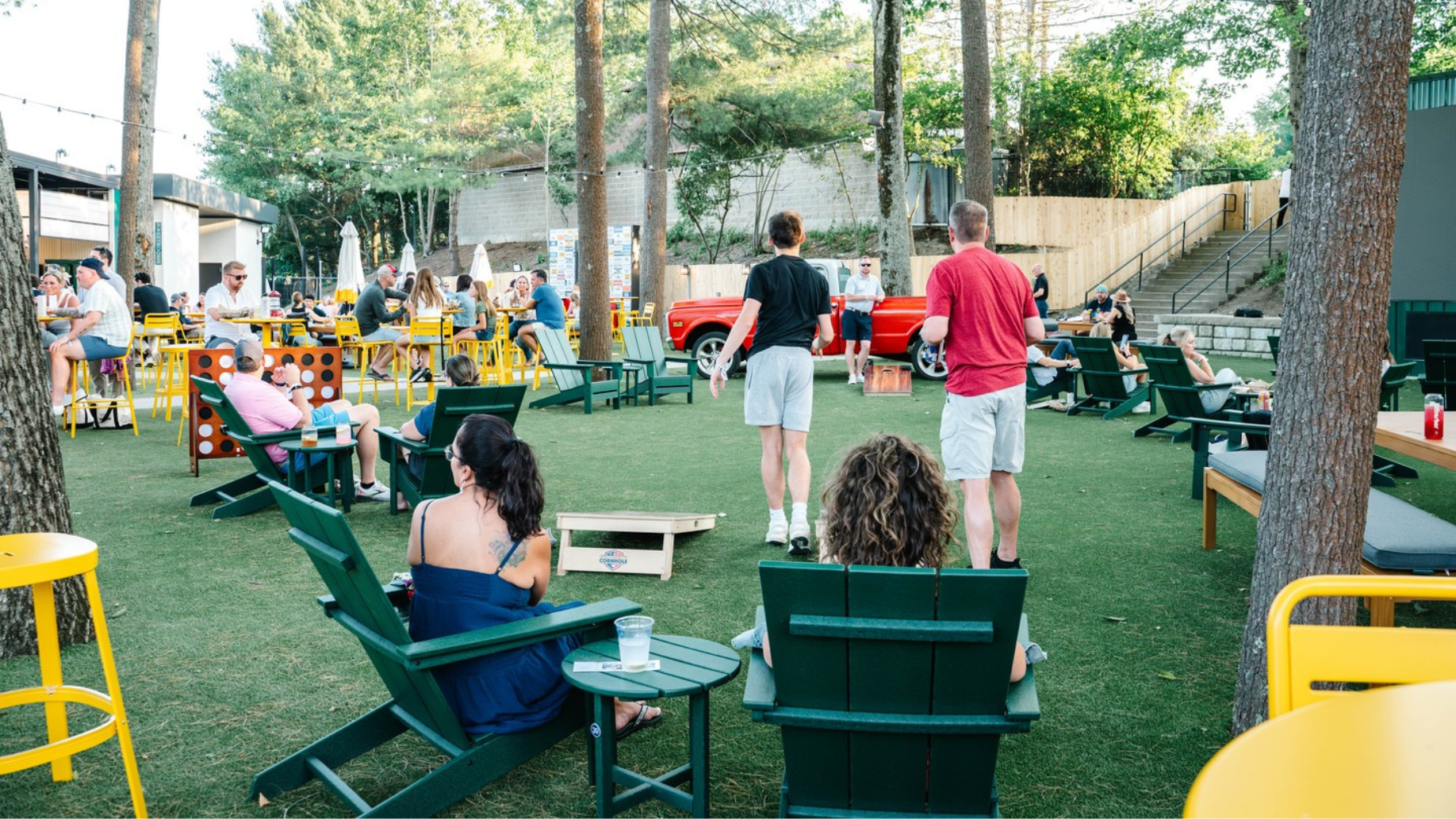 People sitting in outdoor chairs and people playing corn hole 
