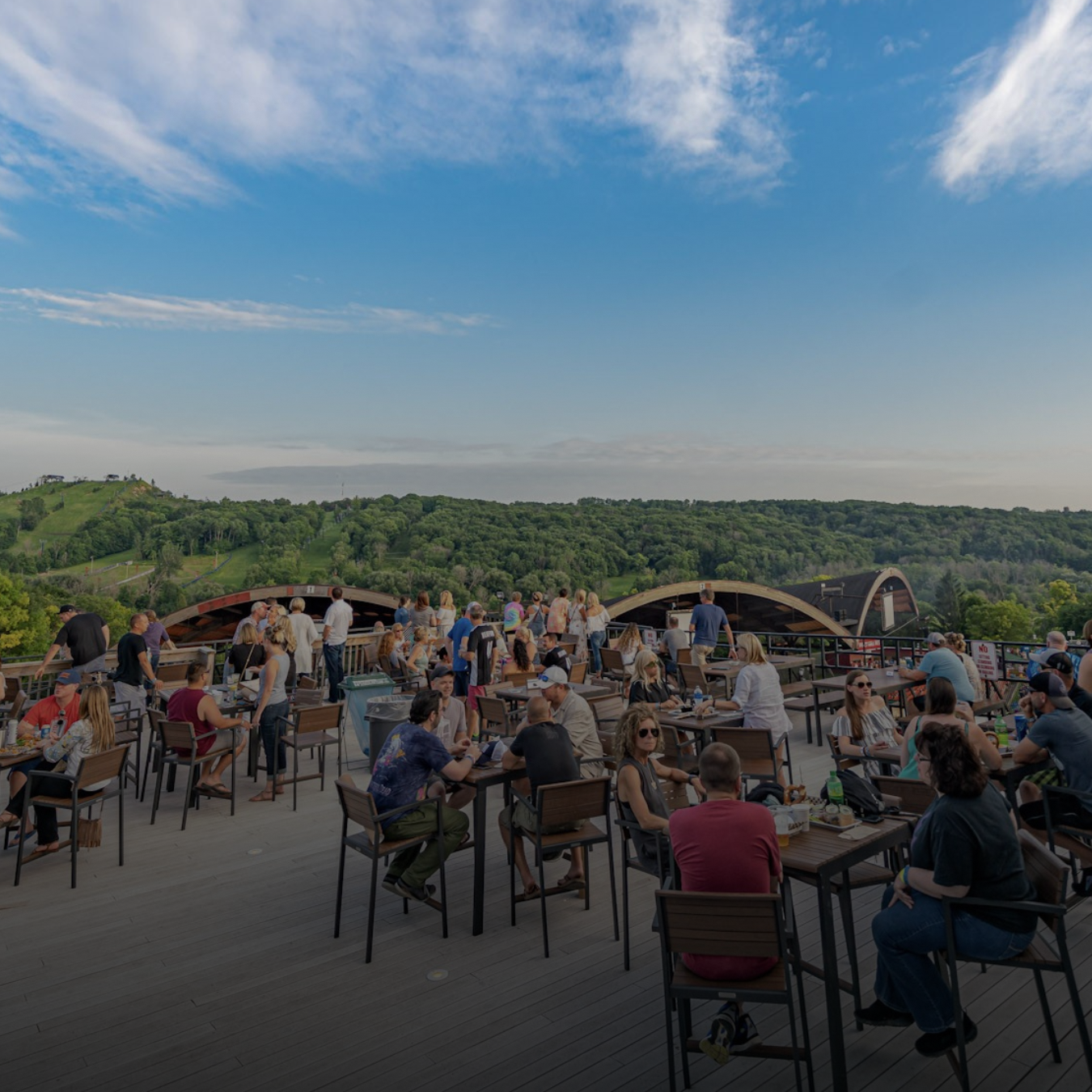 People sitting at tables on an elevated deck overlooking Alpine Valley Music Theatre.