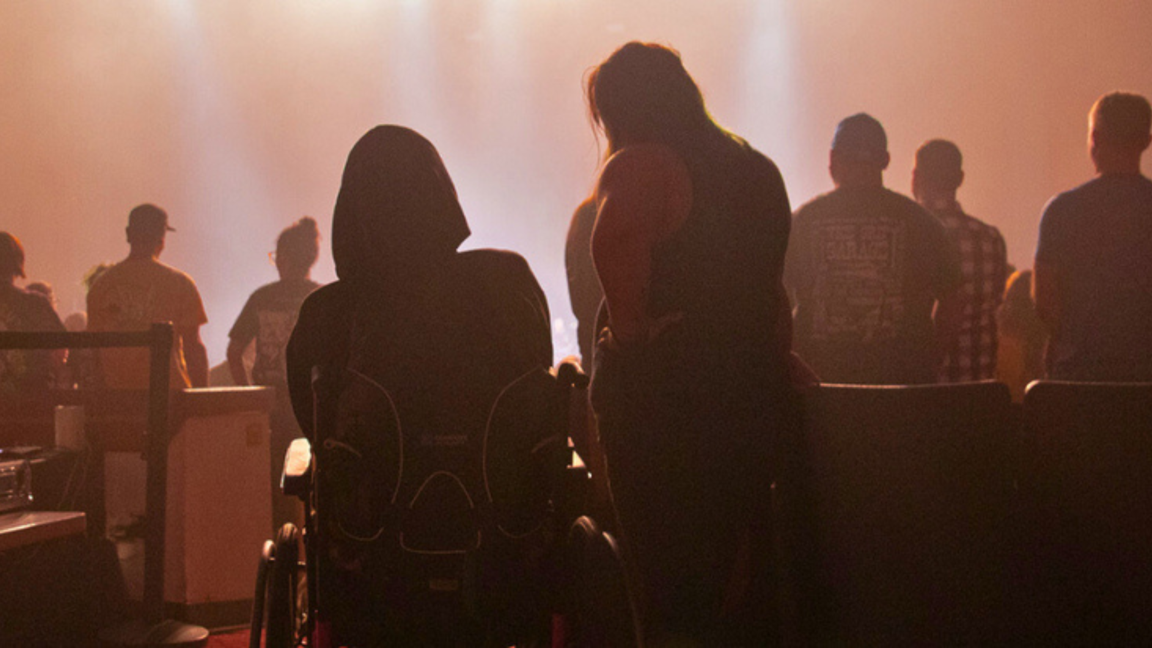 Two people watching a concert. One in a wheelchair and the other standing next to them. 