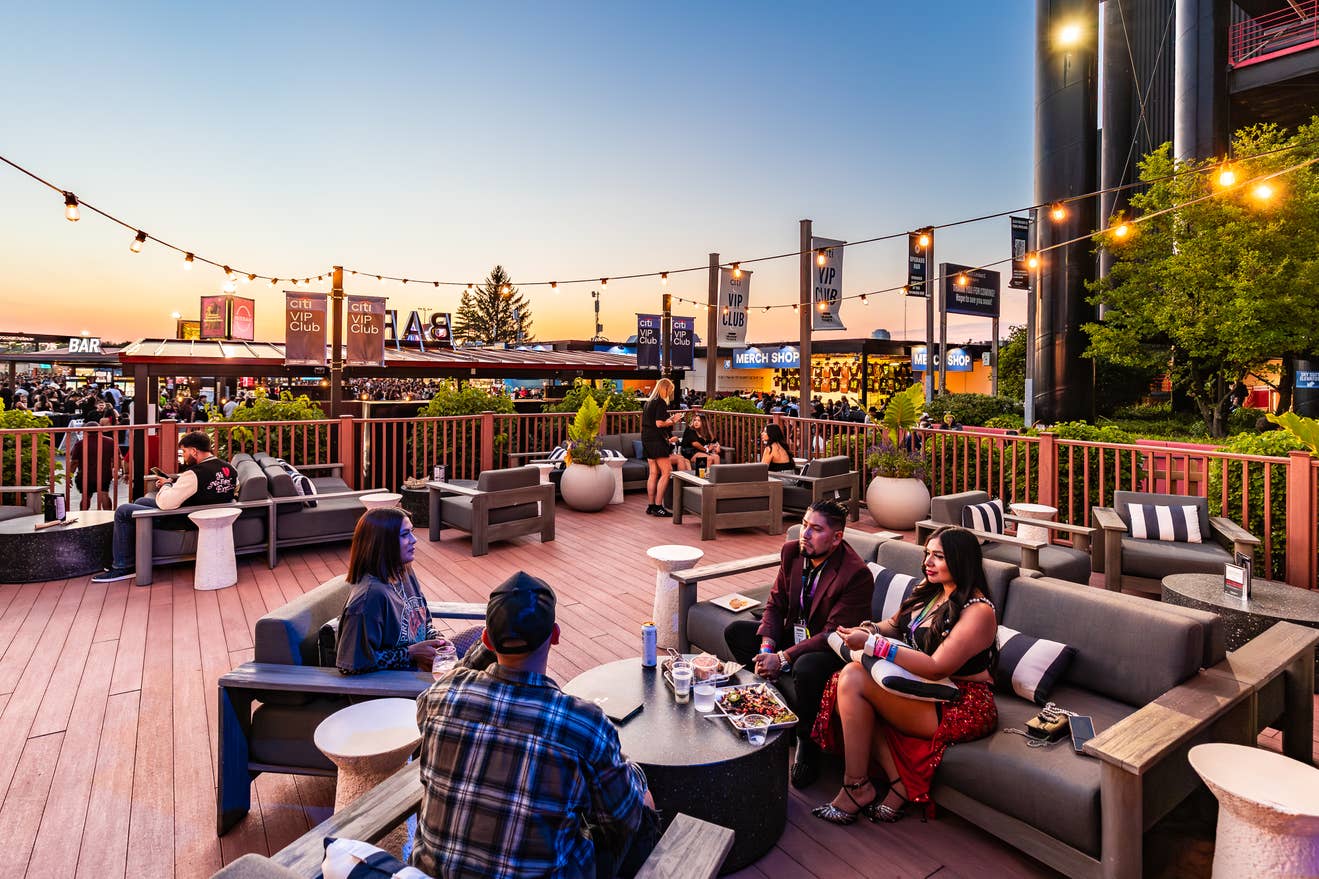 People sit in chairs in outdoor furniture in the VIP Club while a crew member takes their order.