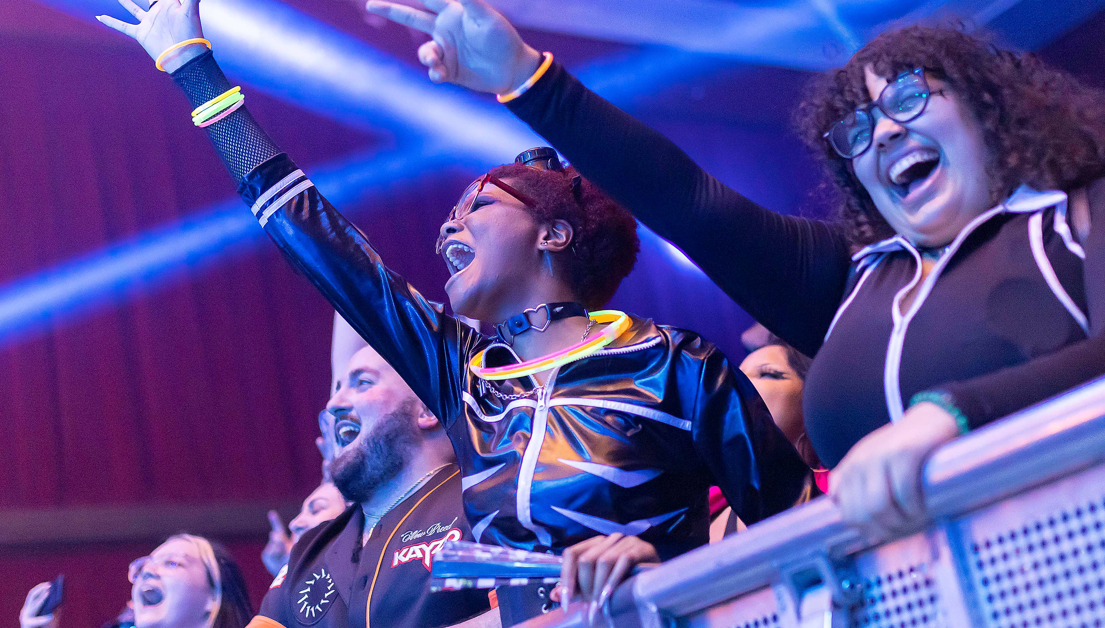 A close up of two girls that are front row at a concert with their right arms in the air pointed toward the stage